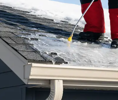 Ice dam removal technician using a steam wand to melt thick ice buildup on a residential roof in Baltimore, MD