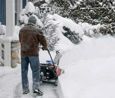 Residential snow removal technician using a snow blower to clear a home driveway and walkway in Baltimore, MD