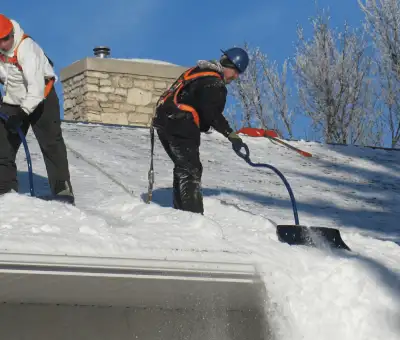 Professional technicians performing roof snow removal with safety harnesses and shovels in Baltimore, MD